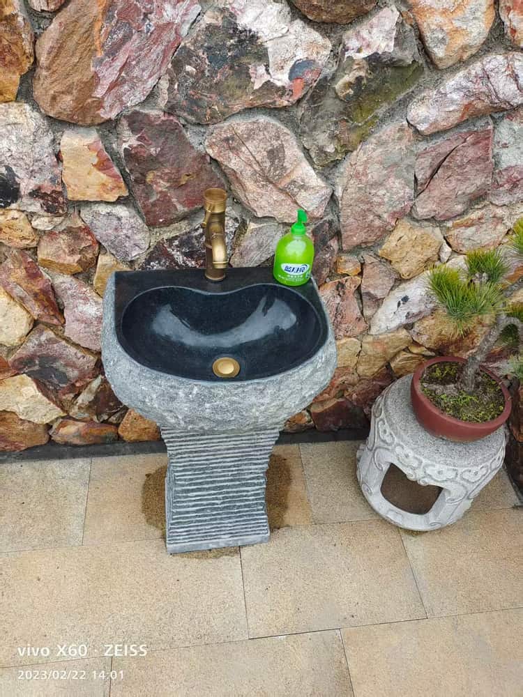 Installed dark stone pedestal basin with decorative support against a stone wall