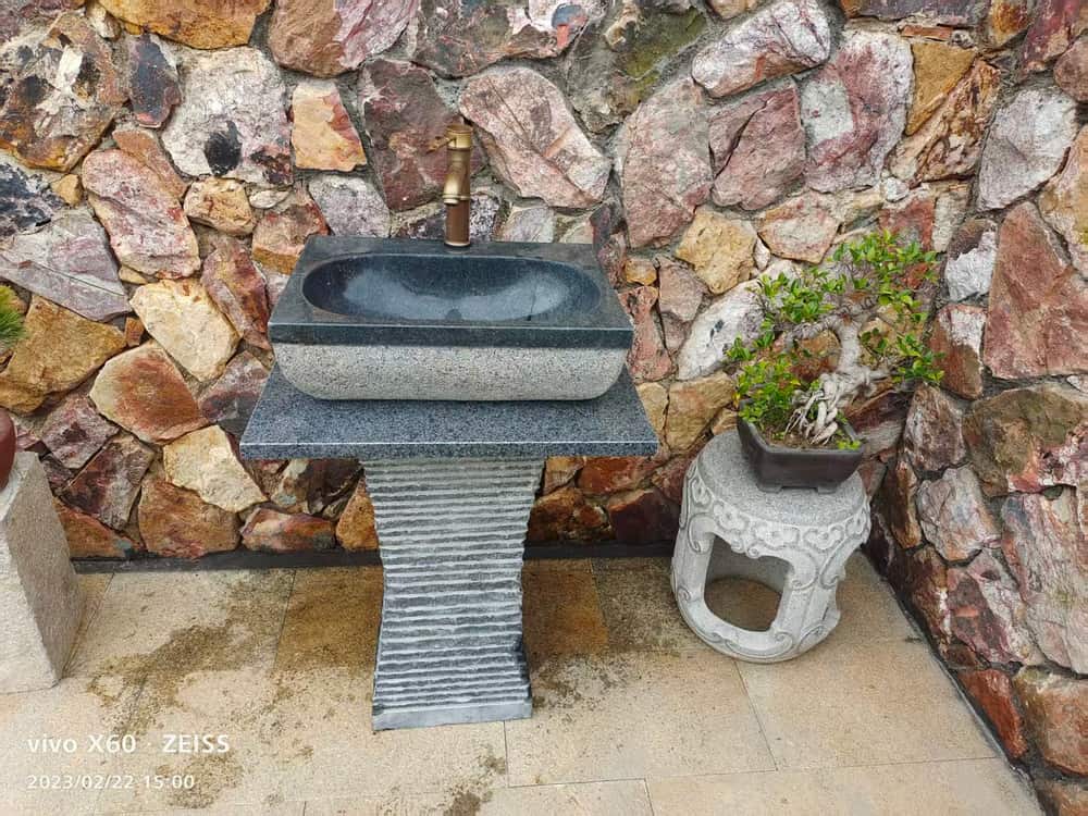 Installed rectangular dark stone pedestal basin against a stone wall