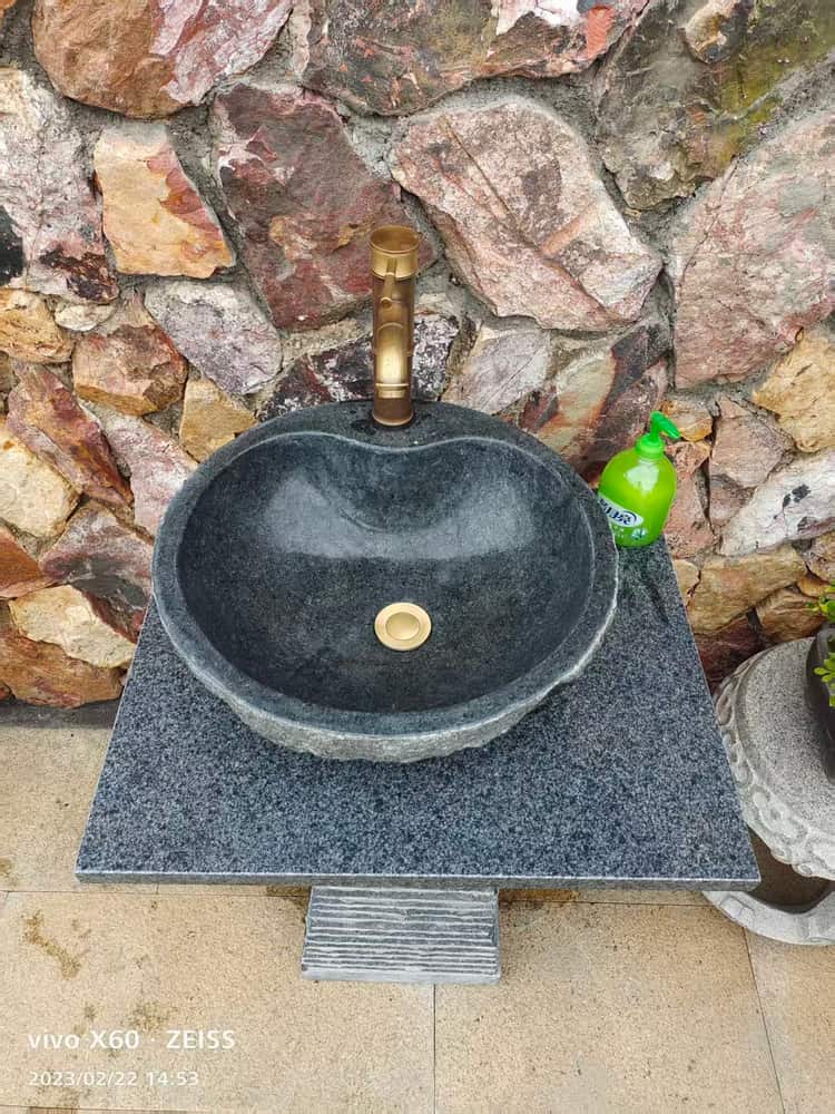 Installed dark stone pedestal wash basin against a stone wall