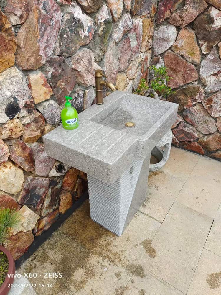 Installed light grey stone pedestal wash basin against a stone wall
