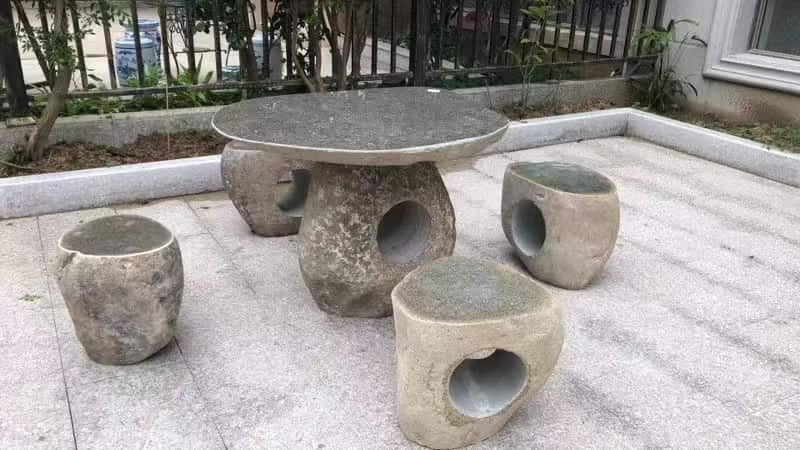 Outdoor stone table with matching stools installed in a paved courtyard