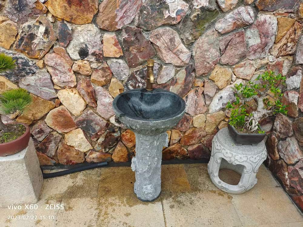 Installed round dark stone pedestal wash basin in a garden setting
